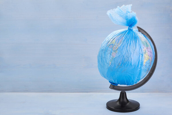 Глобус планеты Земля, одетый в мусорный пластиковый пакет на синем деревянном фоне
