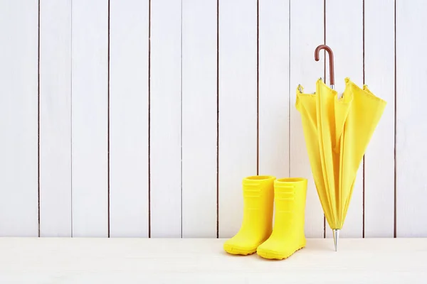 Een paar gele regen laarzen en een paraplu op witte houten achtergrond — Stockfoto