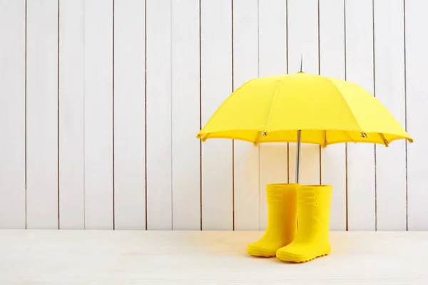 Пара желтых ботинок дождя и зонтик на белом деревянном фоне — стоковое фото