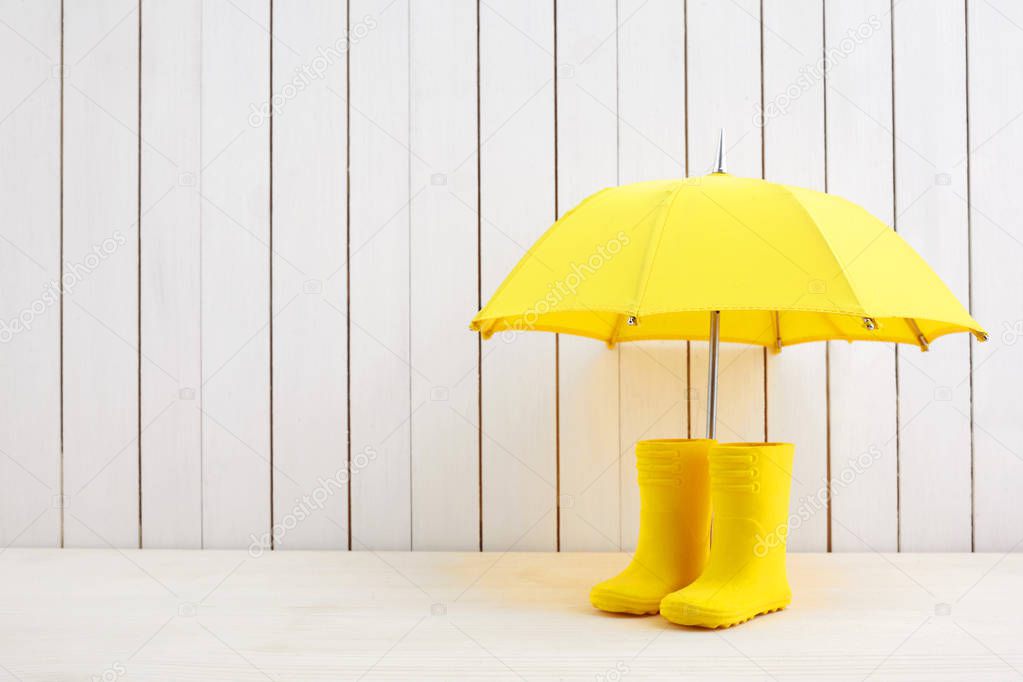 A pair of yellow rain boots and a umbrella on white wooden background
