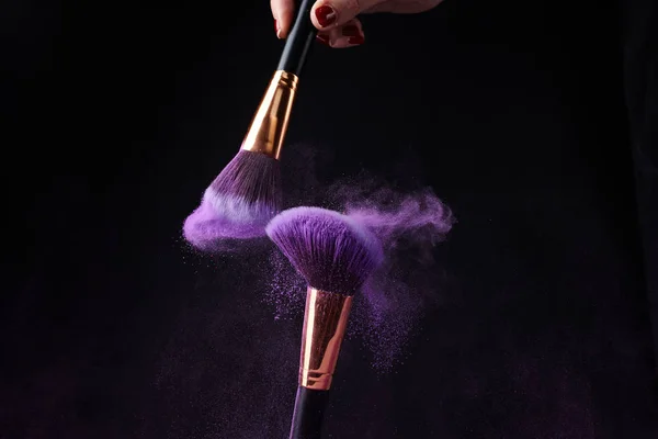 Make-up brushes with silver powder explosion on black background
