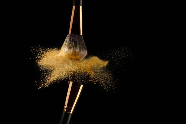 Cosmetische borstel met gouden poeder verspreiden op zwarte achtergrond — Stockfoto