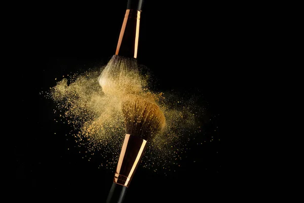 Cosmetic brush with golden powder spreading on black background — Stock Photo, Image