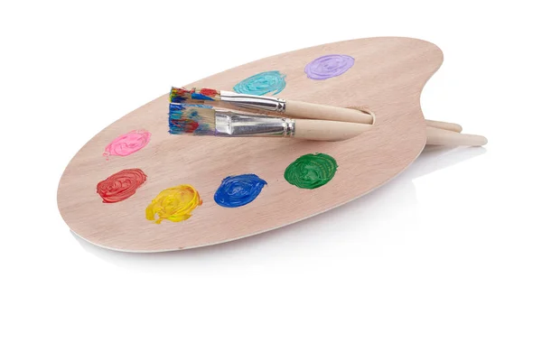 Wooden art palette with blobs of paint and a brush on white back ...