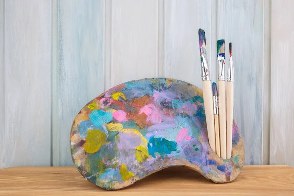 木制艺术调色板，彩色木制背景上有油漆和画笔 — 图库照片