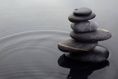 Dalgalı su yüzeyinde suda dengeli kazık zen taşları.