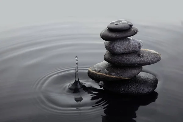 Pietre Zen in pila equilibrata in acqua sulla superficie dell'acqua increspata e goccia d'acqua . — Foto Stock