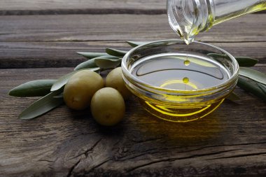 Kaliteli ahşap arka planda bir kaseye zeytinyağı döken şişe.
