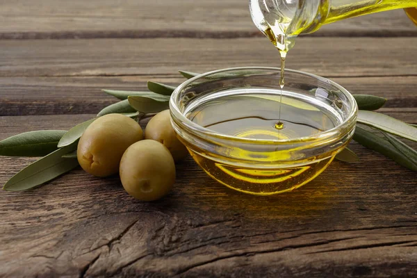 Butelka wlewająca oliwę z oliwek do miski na drewnianym tle vintage — Zdjęcie stockowe