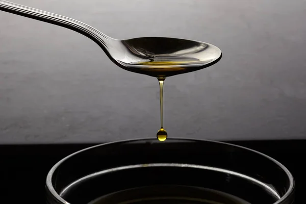 Gocciolano gocce d'olio da un cucchiaio su sfondo scuro — Foto Stock