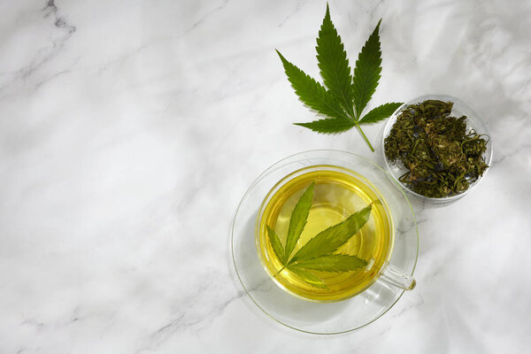 Cannabis herbal tea. Hot drink on light background with hemp leaves.