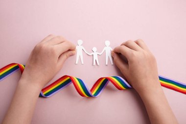 Homoseksüel aile. Farklı bir aile. Kağıt, aile simgesini yağmur kurdelesi ve çocuk elleriyle kesiyor.