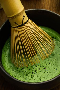 Canlı yeşil kibrit çayını karıştıran bambu çırpıcısı koyu bir kasede köpüklü bir doku yaratıyor..