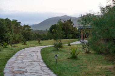 Ağaçların, çimenlerin ve taş yolun yanındaki dağlarda güzel bir dinlenme yeri.