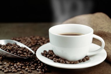 Kavrulmuş kahve çekirdekleri, çanta ve siyah arka planda taş masada kepçe ile beyaz fincan sıcak kahve