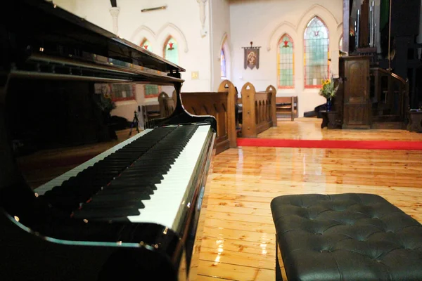 Black grand piano in a church which features some pretty stained glass windows
