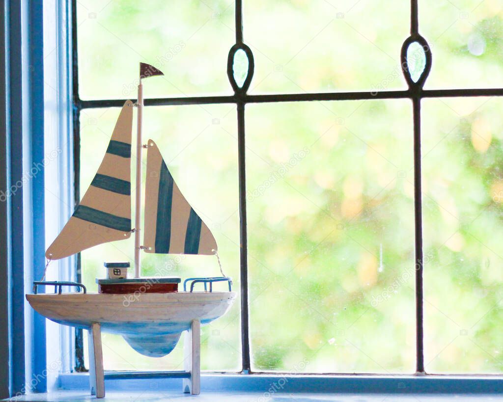 Sailboat ornament in front of lead light window in beach house. Boats are a staple of coastal holiday home decor!