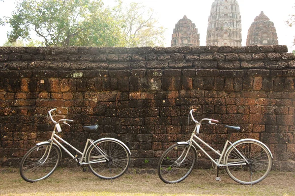 Two bicycles resting outside an ancient wall in Sukhothai Heritage Park, Thailand