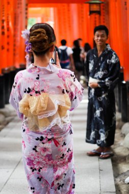 Pamuk yukata giymiş çift Kyoto 'daki Fushimi Inari türbesindeki vermillion torii kapı tünellerinde poz veriyor.
