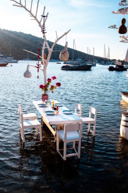 Bodrum, Gumusluk Town 'daki Ege balık lokantası masası. Restoran masaları ve sandalyeler denizde.