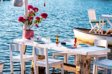 Bodrum, Gumusluk Town 'daki Ege balık lokantası masası. Restoran masaları ve sandalyeler denizde.