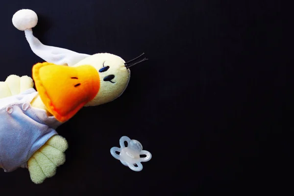 Stuffed duck and pacifier on a black background.