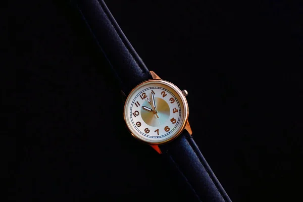 Gold and quartz watch with leather strap on a black background.