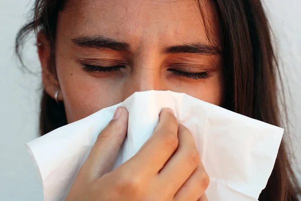 Health and medicine concept - Young woman blowing nose into tissue.