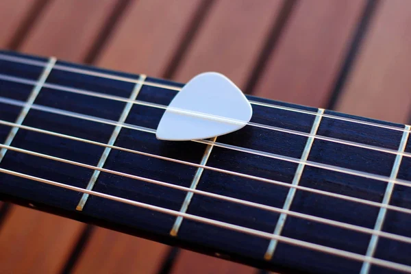 Guitar pick on the fingerboard of a brown guitar.