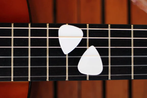 Guitar picks on the fingerboard of a brown guitar.