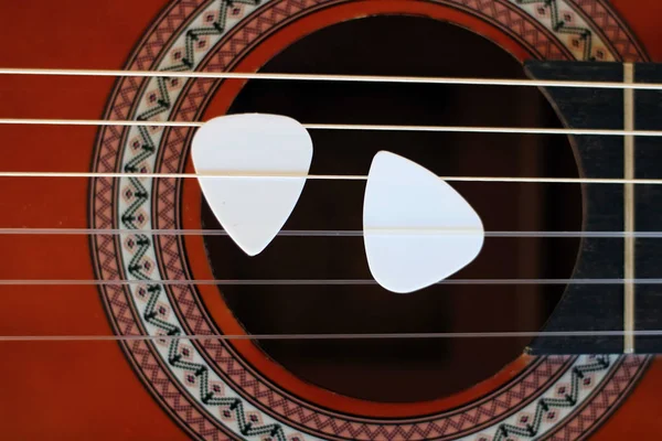 Guitar picks on the fingerboard of a brown guitar.