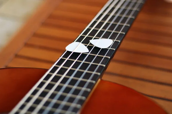 Guitar picks on the fingerboard of a brown guitar.