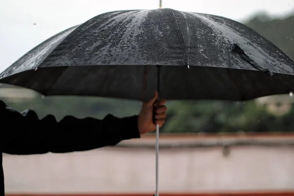 Man with a leather jacket holds open black umbrella in his hand under the rain.