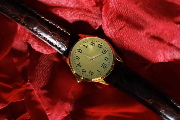 Gold and quartz watch with a leather strap on top of a pair of rose petals.