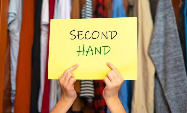 Hands picking up a sign that says Second Hand. Second hand clothing concept. Buy pre-owned clothing.