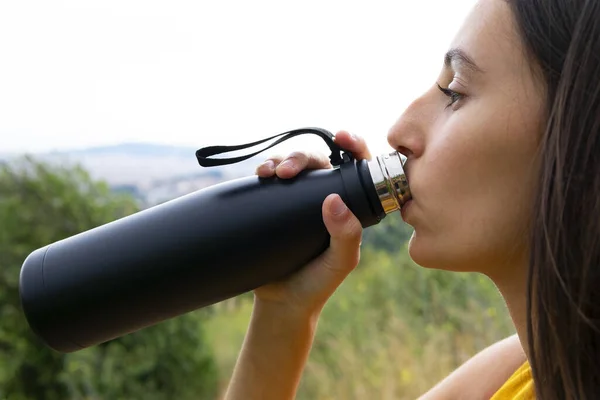 Hiker woman drinking water from a thermos. Concept of hiking in nature and hydration.