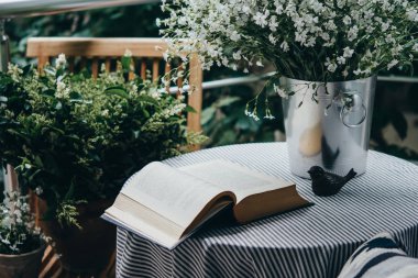 Küçük masa, kitap ve güzel teras ya da balkon çiçekleri