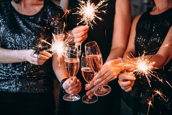 Friends celebrating Christmas or New Year eve party with Bengal lights and rose champagne.