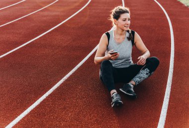 Genç, güzel bir kadın ile onun smartphone bir stadyum koşu parkuru oturma dinlenme sahip.