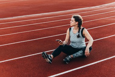 Genç, güzel bir kadın ile onun smartphone bir stadyum koşu parkuru oturma dinlenme sahip.