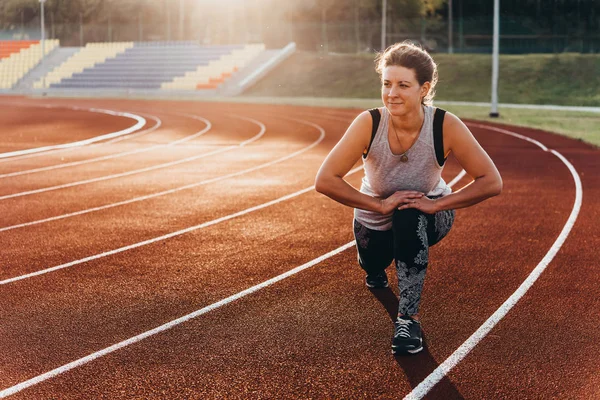 A young beautiful woman is warming up before jogging of exercising at a stadium running track.