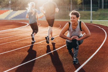 Güzel bir genç kadın bir stadyum koşu parkuru egzersiz koşu önce ısınıyor.