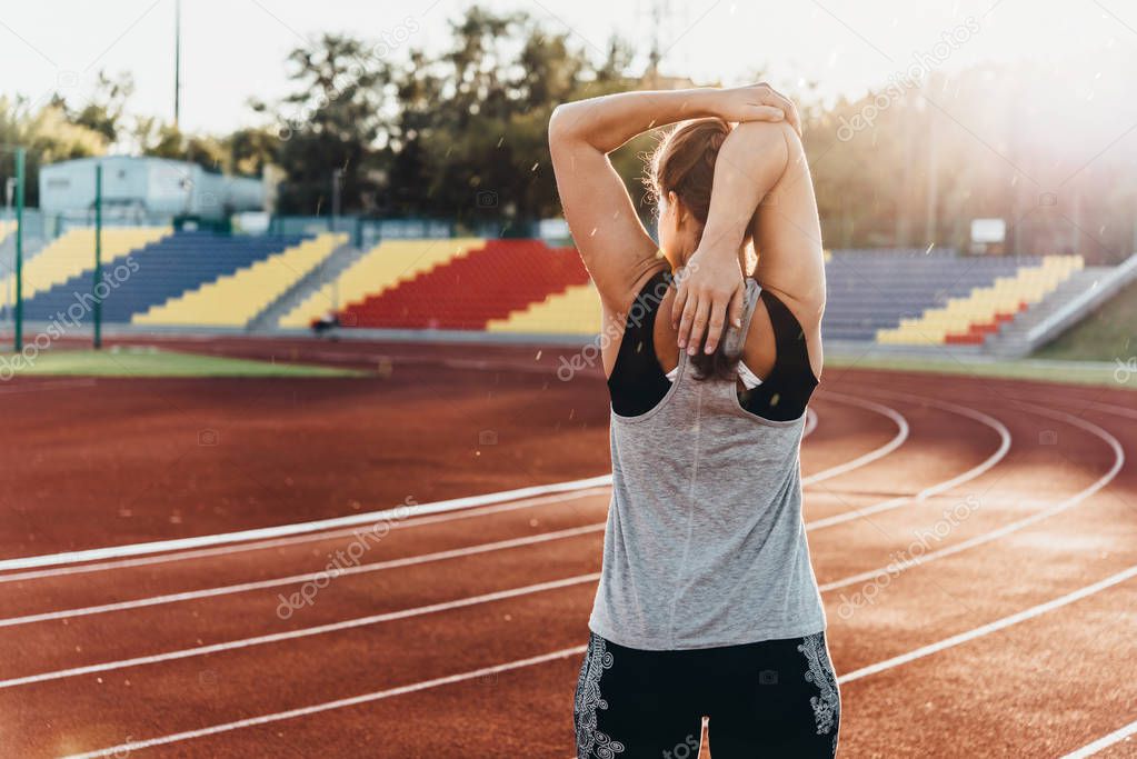 A young beautiful woman is warming up before jogging of exercising at a stadium running track.