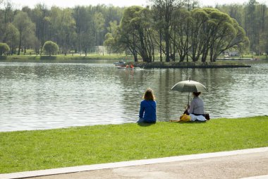 01-05-2018, Russia, Moscow, Tsaritsyno park manor, May holidays in the park, women are resting on the lake on a green lawn. A girl with umbrella sits back