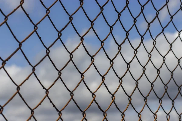 Old rusty mesh netting diagonally against a blue sky with clouds, background wallpaper texture — 스톡 사진