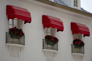 Three beautiful tall windows with red flowers and forged bars and a red canopy on a white wall