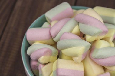 Ahşap masa üzerinde çok renkli spiral marshmallow sehpa kase, yakın plan. Tatlı havadar tatlı, spiral şekil, renk sarı pembe yeşil mavi.