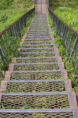 Metal demir merdiven aşağı gidiyor. Metal adımlar demir korkuluklar, yeşil çimenli bir tepeden inen