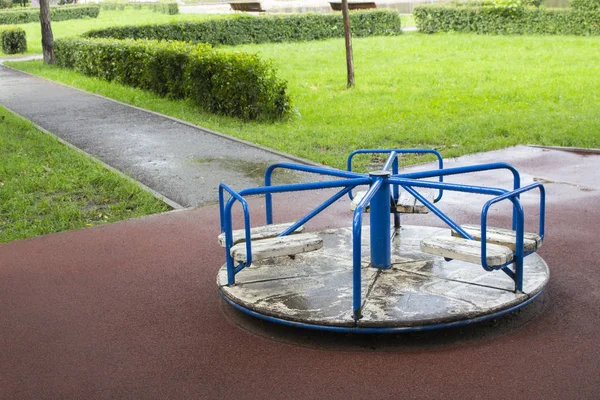 Ein kleines Kinderkarussell nach dem Regen. Spielplatz für Kinder Spiele altes Karussell. blaue Knöpfe, weißer Boden mit abblätternder Farbe — Stockfoto