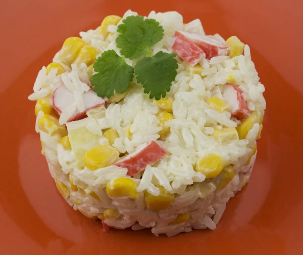 Rice salad with crabs corn with mayonnaise dressing, served on an orange plate and decorated with greens. Elegant salad serving with surimi crab sticks and white boiled rice. — Stock Photo, Image